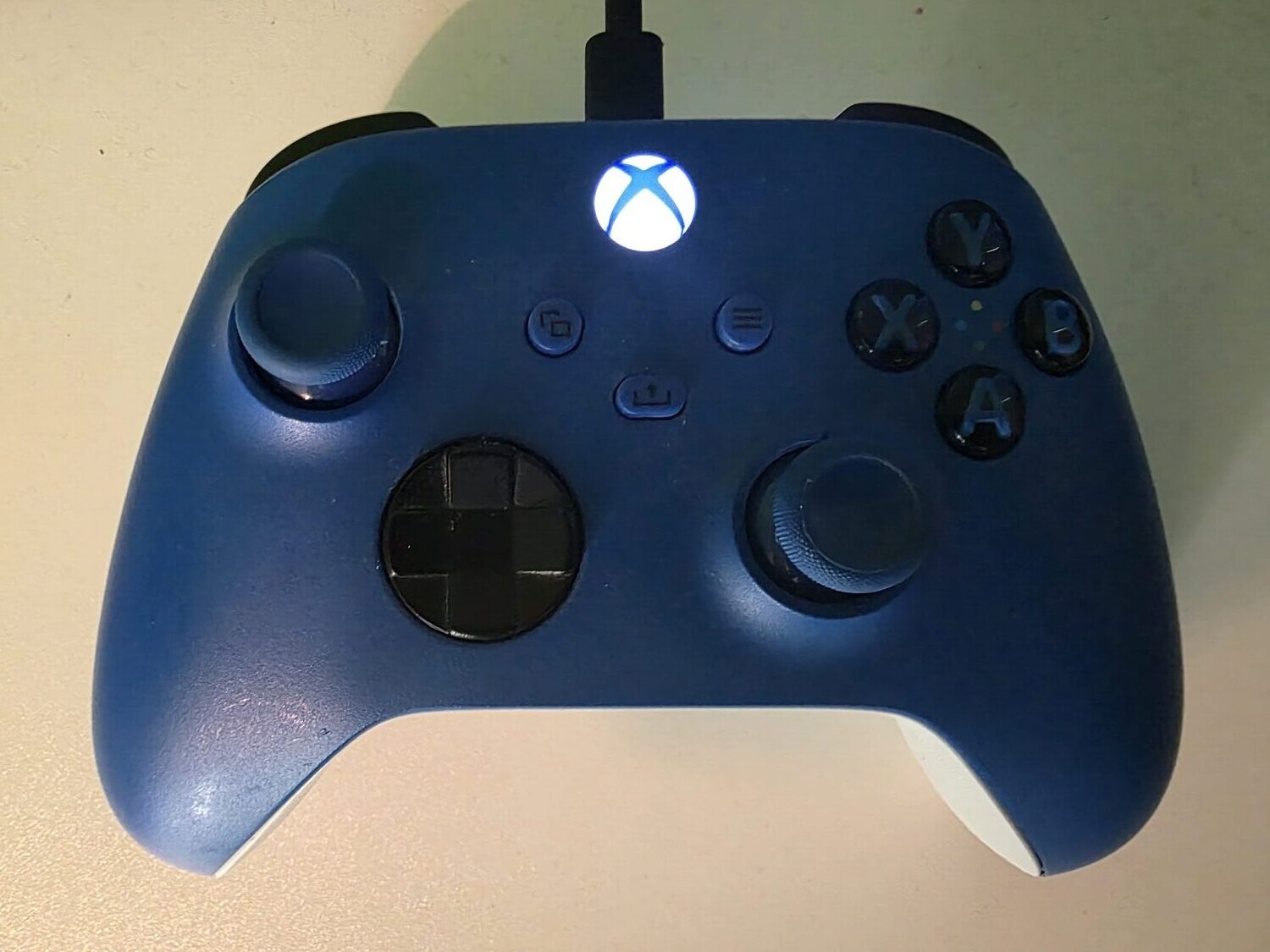 Xbox Wireless Controller in Blau (Shock Blue), per USB-C-Kabel verbunden und mit leuchtender Xbox-Taste
